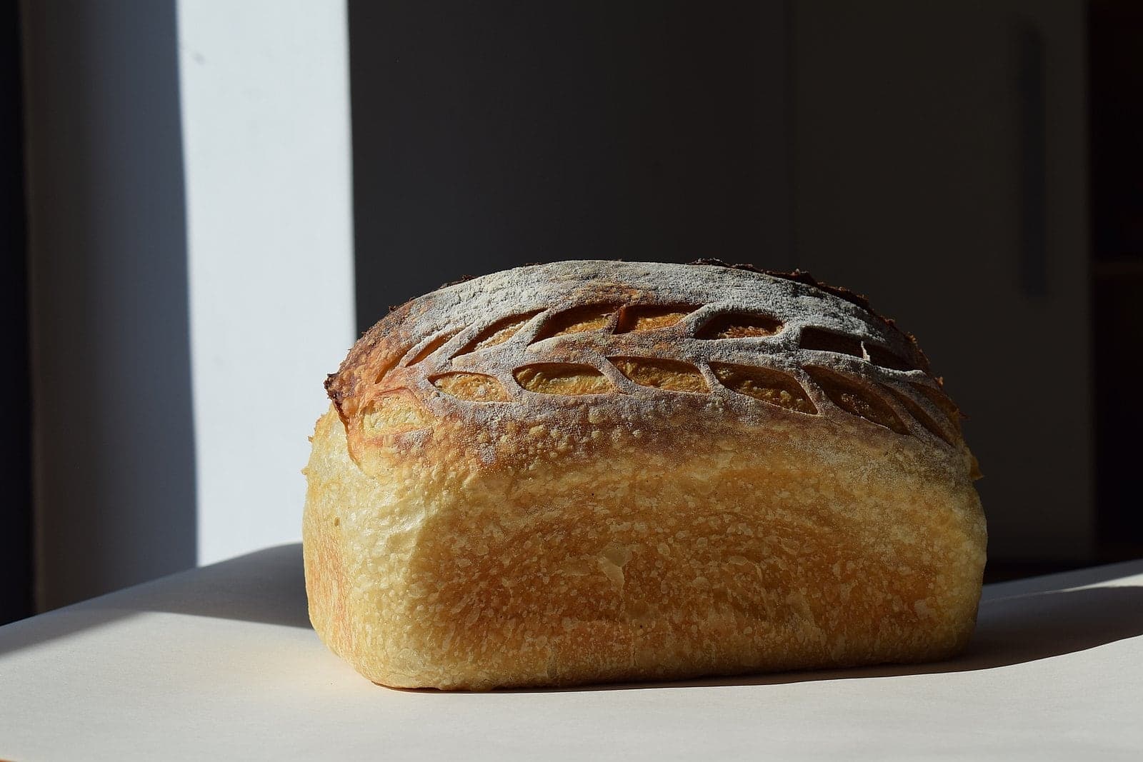 Sourdough white bread with an ear-of-wheat pattern on the crust, in window light.