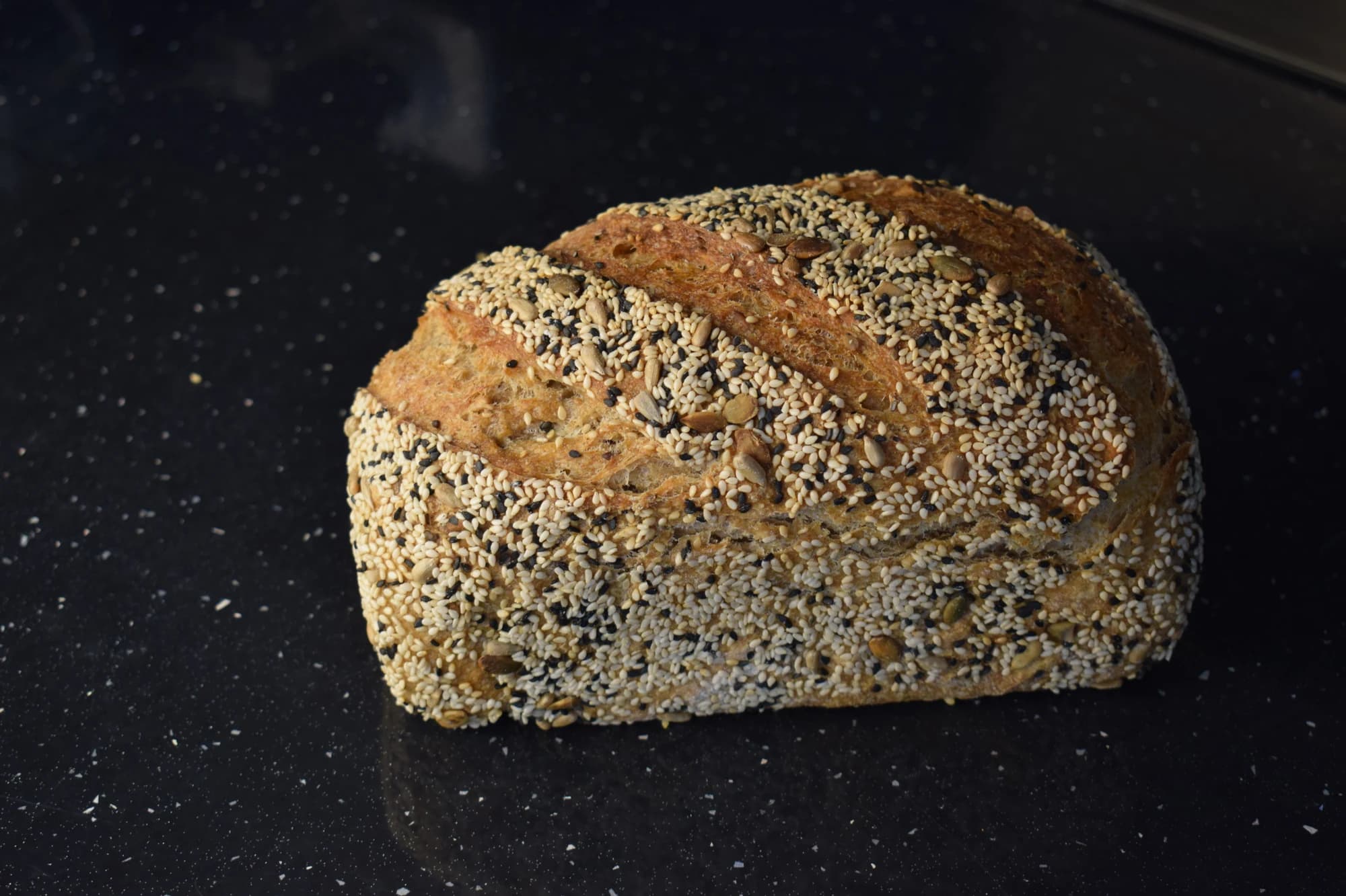 Two white loaves with seeds on a black surface.